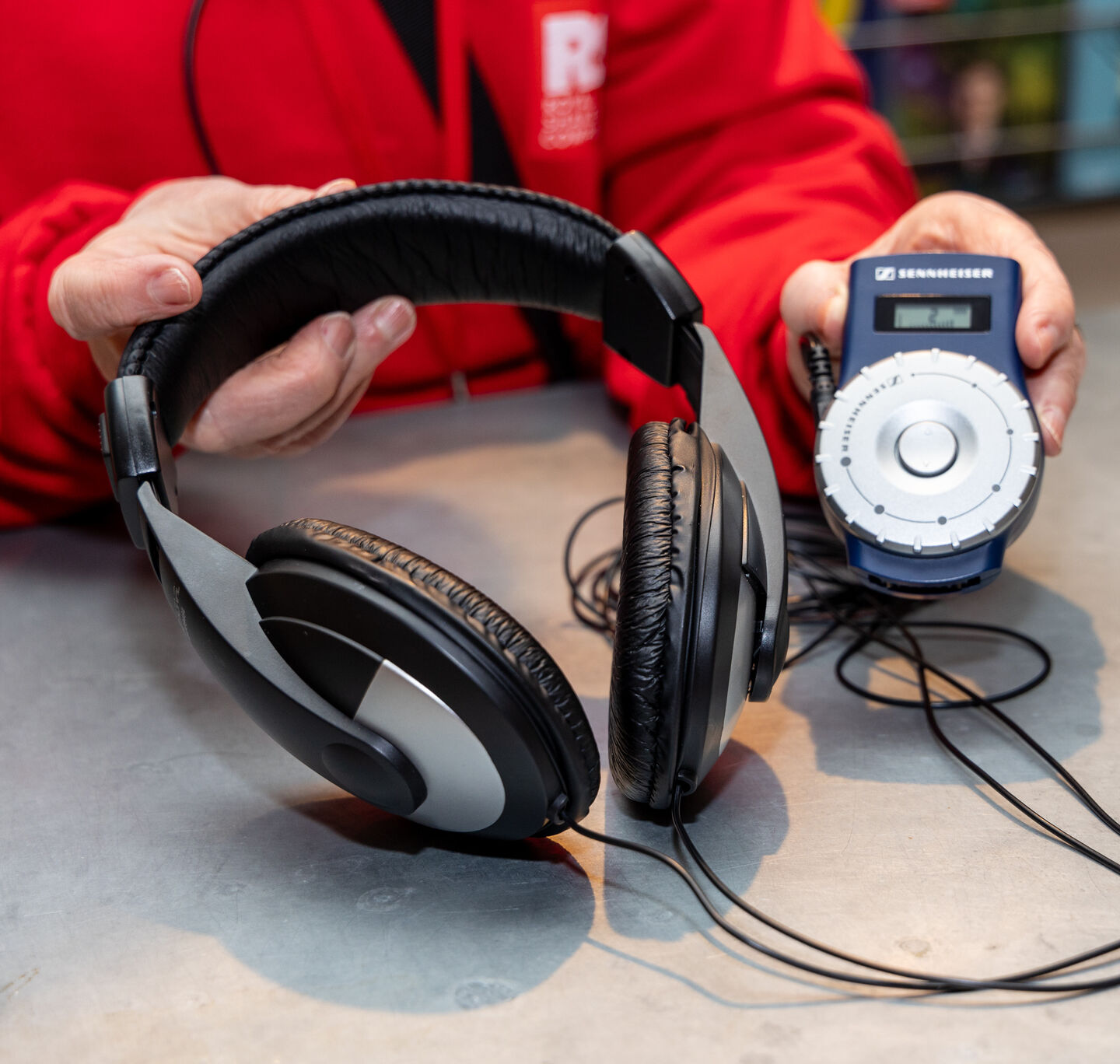 Person wearing an RSC red jacket holds a set of headphones and audio player